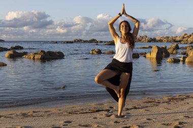 Latin seksi kadın gün batımında plajda yoga yapıyor.