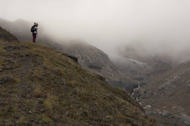 Kazbek tepesi yakınlarındaki sisli yaz gününde Kafkasya dağlarında yürüyüş yapan bir kadın.
