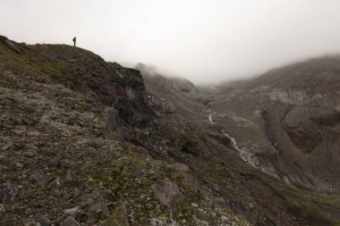 Kazbek tepesi yakınlarındaki sisli yaz gününde Kafkasya dağlarında yürüyüş yapan bir kadın.