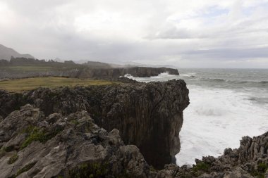 Asturias 'ta Bufones de Pria' nın manzarası bulutlu bir günde dalgalı denizler ve kıyılarda dalga spreyi