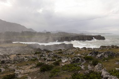 Asturias 'ta Bufones de Pria' nın manzarası bulutlu bir günde dalgalı denizler ve kıyılarda dalga spreyi