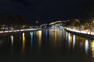 Tiflis şehir merkezinin panoramik manzarası. Geceleri kilise ve nehir üzerinde barış köprüsü. 