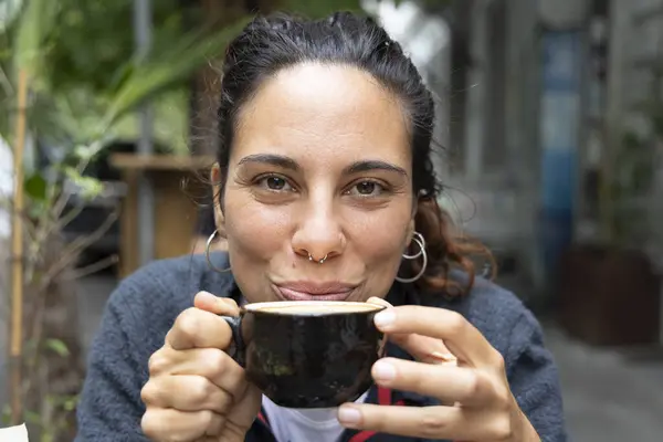 Portrait of young hispanic woman drinking coffee outside alone smiling