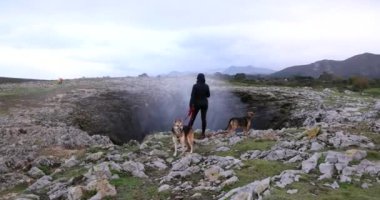 Bulutlu bir günde İspanya 'da Bufones de Pria hava deliğinde iki köpeği olan genç bir kadın.