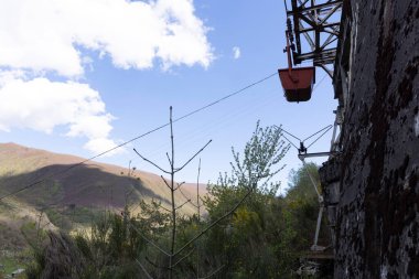 Kömür madenciliği arabası halatla halat üzerinde dağlarda terk edilmiş endüstriyel ekipmanlar açık güneşli bir günde mavi gökyüzü ve bahar çiçeği çayırında.