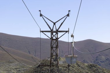 Terk edilmiş endüstriyel kömür madeni arabası kabloyla birlikte paslı metal kuleyle güneşli bir bahar gününde çiçek çayırı ve mavi gökyüzü ile birlikte.