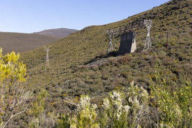 Tormaleo 'daki Asturias dağlarındaki sanayi kömür madenciliği kablolarından kuleleri olan terk edilmiş çelik yapı güneşli bir bahar günü çiçeklerle dolu.