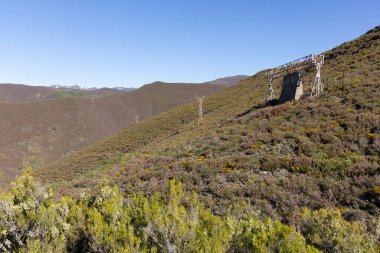 Tormaleo 'daki Asturias dağlarındaki sanayi kömür madenciliği kablolarından kuleleri olan terk edilmiş çelik yapı güneşli bir bahar günü çiçeklerle dolu.