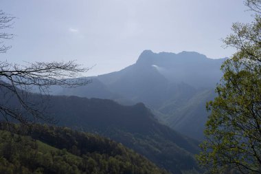 İspanya 'nın kuzeyindeki Picos de Europa Ulusal Parkı' nda yeşil bitki örtüsü ve mavi gökyüzü ile aydınlık güneşli bir bahar gününde tepe ve bulutlu dağ manzarası.