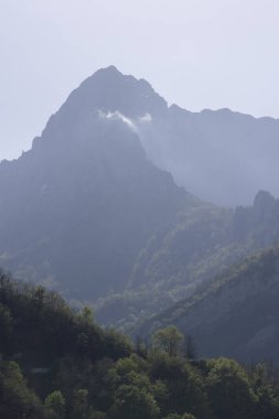 İspanya 'nın kuzeyindeki Picos de Europa Ulusal Parkı' nda yeşil bitki örtüsü ve mavi gökyüzü ile aydınlık güneşli bir bahar gününde tepe ve bulutlu dağ manzarası.