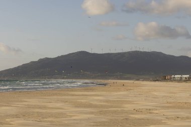 Güneşli bir günde okyanusta sörf yapan uçurtma sörfçüleriyle Tarifa sahilinin manzarası.