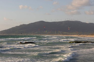 Parlak güneşli bir günde, Tarifa sahilinde bulutlarla sörf yapan birçok insan uçurtma sörfü yapar..