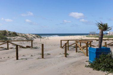 Zahara de los Atunes plajı. Teknesi ve kumulları üzerinde çiçekleri olan mavi gökyüzü ve bulutlarıyla güneşli bir yaz günü..