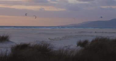 Uçurtma sörfçülerinin gün batımında okyanusta sörf ve sörf yaparken soldan sağa doğru dönen manzara..