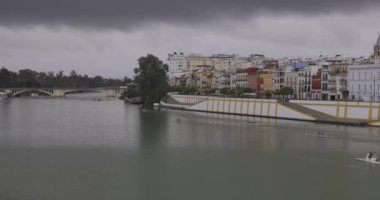 Karanlık gökyüzü ve bulutlu bir günde Sevilla 'daki ev ve nehrin panoramik manzarası.