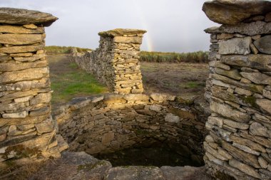 Doğa, tarih ve insan hayatı arasındaki bağlantıyı sembolize eden, sakin bir kırsal alan tarafından çerçevelenmiş yıpranmış bir taşın görüntüsü..