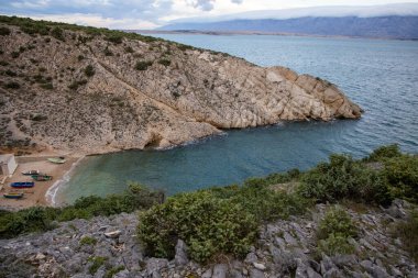 Bu görüntü kayalık kayalıkların, berrak mavi suların ve gözlerden uzak küçük teknelerin olduğu sakin bir sahil manzarası yakalıyor. Huzur ve doğal güzelliği çağrıştırıyor..