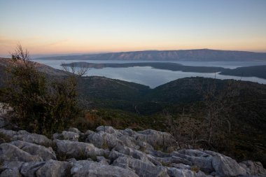 Alacakaranlıktaki panoramik manzara, nefes kesen kıyı manzarasını ve dingin suları yakalar. Günden geceye resim gibi doğal bir ortamda geçişi vurgular..