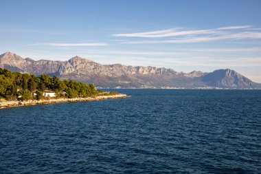 Bu nefes kesen kıyı manzarası, arka plandaki huzurlu dağları yakalar. Rahatlamayı ve keşifleri davet eden bir huzur ve doğal güzellik hissi verir..