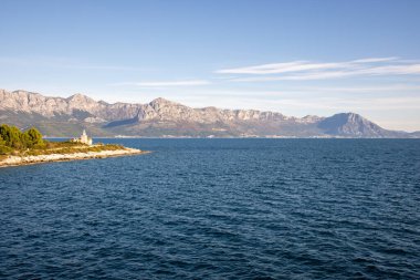 Bu görüntü, doğal güzelliği ve deniz kıyısındaki ahenkli yaşamı simgeleyen görkemli bir sahne sunan görkemli bir dağ zeminine sahip huzurlu bir sahil köyünü gösteriyor..