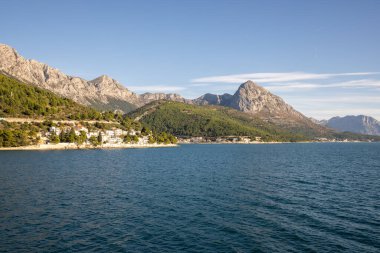 Etkileyici dağlarla çevrili sakin bir kıyı şeridinin nefes kesici manzarası doğanın güzelliğini gözler önüne seriyor ve sudaki sükuneti davet ediyor..