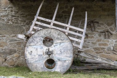 Çürümüş taş bir duvara yaslanmış büyük dairesel bir tekerleği olan antika ahşap bir araba, tarihi tarım araçları sergiliyor..