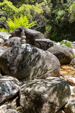 Görüntü, birkaç büyük gri kayanın yakın çekimini gösteriyor. Kayalar doku ve boyutta değişimler sergiler. Daha küçük bir taş yığını, büyük kayalardan birinin üzerinde tehlikeli bir şekilde dengelenmiştir..