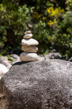Daha büyük, koyu gri bir kayanın üzerinde titizlikle dengelenmiş dört taştan oluşan küçük bir yığının yakın plan çekimi. Taşlar açık gri ve kahverengi lekeli, çeşitli doku ve şekiller sergiliyorlar..