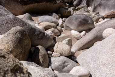 Yüksek açılı, yakın plan, çeşitli boyutlarda yuvarlak kaya ve taş koleksiyonu. Kayalar hem pürüzsüz hem de pürüzsüz yüzeyleri gösteren doku değişiklikleriyle gri ve açık gri renkler sergiliyor.. 