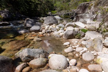 Yüksek açılı, sığ bir dere yatağının yakın görüntüsü esasen çeşitli kaya ve çakıl taşlarından oluşmuş. Su nispeten temiz, dere yatağının görünmesini sağlıyor.. 