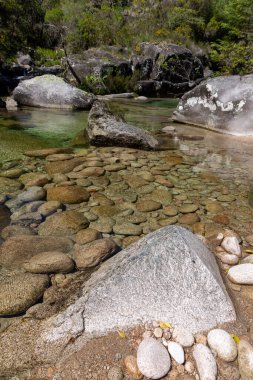 Yüksek açılı, yakın çekim bir nehir yatağı, esasen çeşitli boyutlarda yuvarlak, pürüzsüz taşlardan oluşan kahverengi ve gri tonlarda. Taşlar yoğun bir şekilde bir araya toplanır ve dokulu bir yüzey oluşturur..