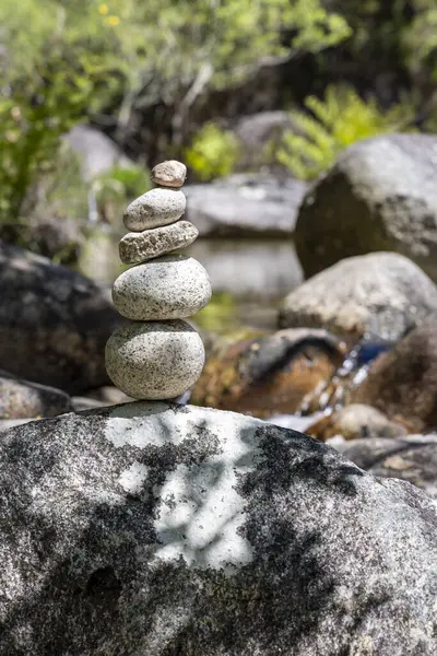 Yakın plan bir fotoğraf dikkatlice dengelenmiş gri ve açık gri yuvarlak taşlar yığınını tasvir eder. Taşlar çeşitli boyutlarda ve şekillerde, pürüzsüz ve pürüzsüz dokuları arasındaki kontrast üzerinde duruluyor.. 