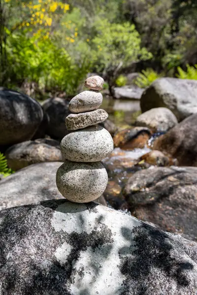 Dört gri ve beyaz taştan oluşan dikey yığını üst üste dengeleyen yakın plan bir çekim. Taşların dokuları değişkendir, bazıları daha pürüzsüz yüzeyler gösterir ve diğerleri daha pürüzsüz görünür.. 