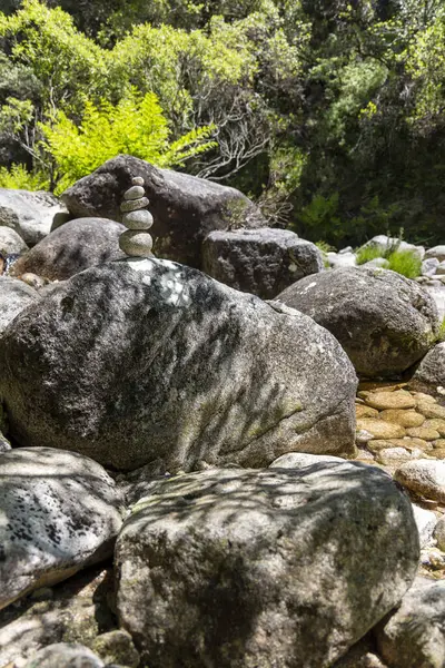 Görüntü, birkaç büyük gri kayanın yakın çekimini gösteriyor. Kayalar doku ve boyutta değişimler sergiler. Daha küçük bir taş yığını, büyük kayalardan birinin üzerinde tehlikeli bir şekilde dengelenmiştir..