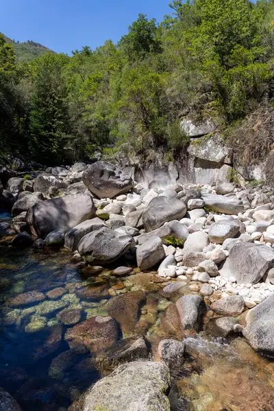 Görüntü, çeşitli boyutlarda açık gri, beyaz kaya ve kayalardan oluşan bir dere yatağının yüksek açılı ve yakın çekim görüntüsünü sergiliyor. Kayalar kaba bir doku ve düzensiz şekiller sergiler..