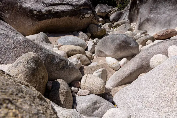 Nehir yatağındaki taşların ve kayaların değişik boyutlarda ve şekillerde olduğu yüksek açılı, yakın çekim görüntüsü. Taşlar ağırlıklı olarak gri ve açık gri tonlarıdır, pürüzsüz ve pürüzsüz dokuların bir karışımını sergiler..
