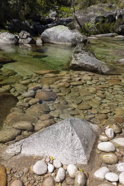 Yüksek açılı, bir nehir yatağının yakın görüntüsü esasen kayaların ve taşların çeşitli boyutları ve şekillerinden oluşuyor. Taşlar hem pürüzsüz hem de pürüzsüz dokular sergileyerek açık kahverengiden koyu kahverengiye ve yeşil renge kadar değişirler.. 