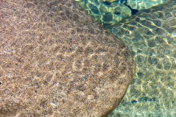 Yakın çekim batık bir taşın detaylı dokusunu ortaya çıkarır. Taşın yüzeyi çeşitli desenler ve düzensizlikler sergiliyor. İnce renk değişimleri derinlik ve mineral bileşimini gösteriyor..  