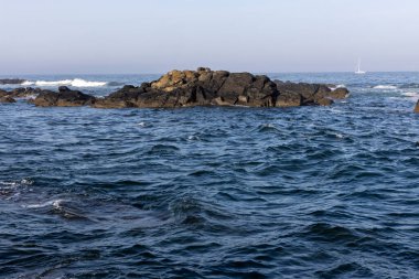 Görüntü, okyanusun koyu mavi suyu olan bir bölümünün geniş açısını gösteriyor. Küçük, karanlık kayalar sudan çıkar ve merkeze yakın küçük bir küme oluşturur..