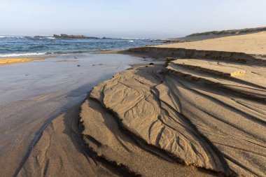 Yüksek açılı, uzun menzilli bir nehir kenarı aşınma ve tortu gösteriyor. Görüntü, nehir kıyısı boyunca birikmiş koyu ve açık kahverengi çökeltilerin karmaşık desenlerini gösteriyor..