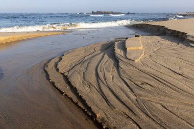 Kumsaldaki kum desenlerine yakından bak. Görüntü, ıslak kuma muhtemelen su akışından oluşmuş karmaşık çizgiler ve kıvrımlar gösteriyor. Kum koyu kahverengi / gri renktedir.