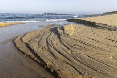 Yüksek açılı, kıyı kayaları oluşumuna yakın çekim. Görüntü, tortu tabakalarının kahverengi ve bronz tonlarında karmaşık desenlerini gösteriyor. Kayalar görünür erozyon sergiliyor..