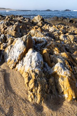 Kum ve kayalardan oluşan bir koleksiyonun yakından çekimi. Kayalar çeşitli dokular sergilerken, bazı bölgeler pürüzsüz, bazıları ise pürüzlü ve yıpranmış görünüyor. Renkler öncelikli olarak toprak tonlarıdır..