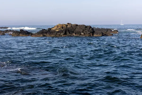 Görüntü, okyanusun koyu mavi suyu olan bir bölümünün geniş açısını gösteriyor. Küçük, karanlık kayalar sudan çıkar ve merkeze yakın küçük bir küme oluşturur..