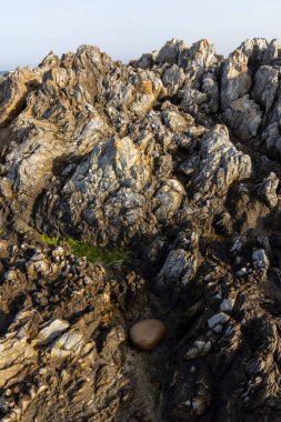 Koyu ve açık renkli taşların bir karışımını gösteren bir kaya yüzeyinin yakın çekimi. Doku pürüzlü ve düzensiz, kayaların şekil ve boyutlarındaki değişimleri gösteriyor. Görüntü ağırlıklı olarak karanlık.