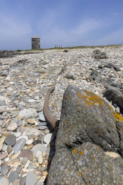 Yüksek açılı, paslı, yıpranmış metal bir nesnenin yakın çekim görüntüsü kısmen kayalık bir plaja gömülmüş. Nesne uzun, ince bir metal parçası gibi görünüyor. Muhtemelen bir makine ya da enkaz parçası.. 