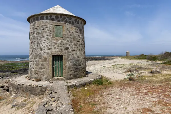 Görüntü, kıyı bölgesinde küçük yuvarlak bir taş kuleyi gösteriyor. Kule yaşlanmış ve yıpranmış görünüyor, konik bir çatısı var. Taş işçiliği sert ve düzensiz. Üzerinde küçük yeşil bir kapı görünür.