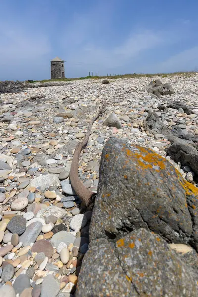 Yüksek açılı, paslı, yıpranmış metal bir nesnenin yakın çekim görüntüsü kısmen kayalık bir plaja gömülmüş. Nesne uzun, ince bir metal parçası gibi görünüyor. Muhtemelen bir makine ya da enkaz parçası.. 