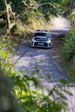 13 Haziran 2025 'te İspanya' da dar, çakıllı ve yemyeşil bitki örtüsüyle çevrili bir yoldan geçen bir ralli aracının orta açı çekimi..