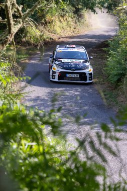 Ourense, İspanya, 13 Haziran 2025: Görüntü, yemyeşil bitki örtüsüyle çevrili dar, dolambaçlı bir asfalt yolda ilerleyen bir ralli aracının yakın görüntüsünü gösteriyor.